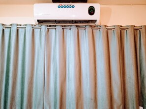 Un appareil de climatisation blanc, doté d’un écran numérique et de boutons de réglage de la vitesse, est placé au-dessus d’un rideau à rayures.