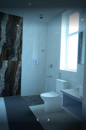 Un baño moderno con pared de mármol, inodoro, lavamanos y ducha.
