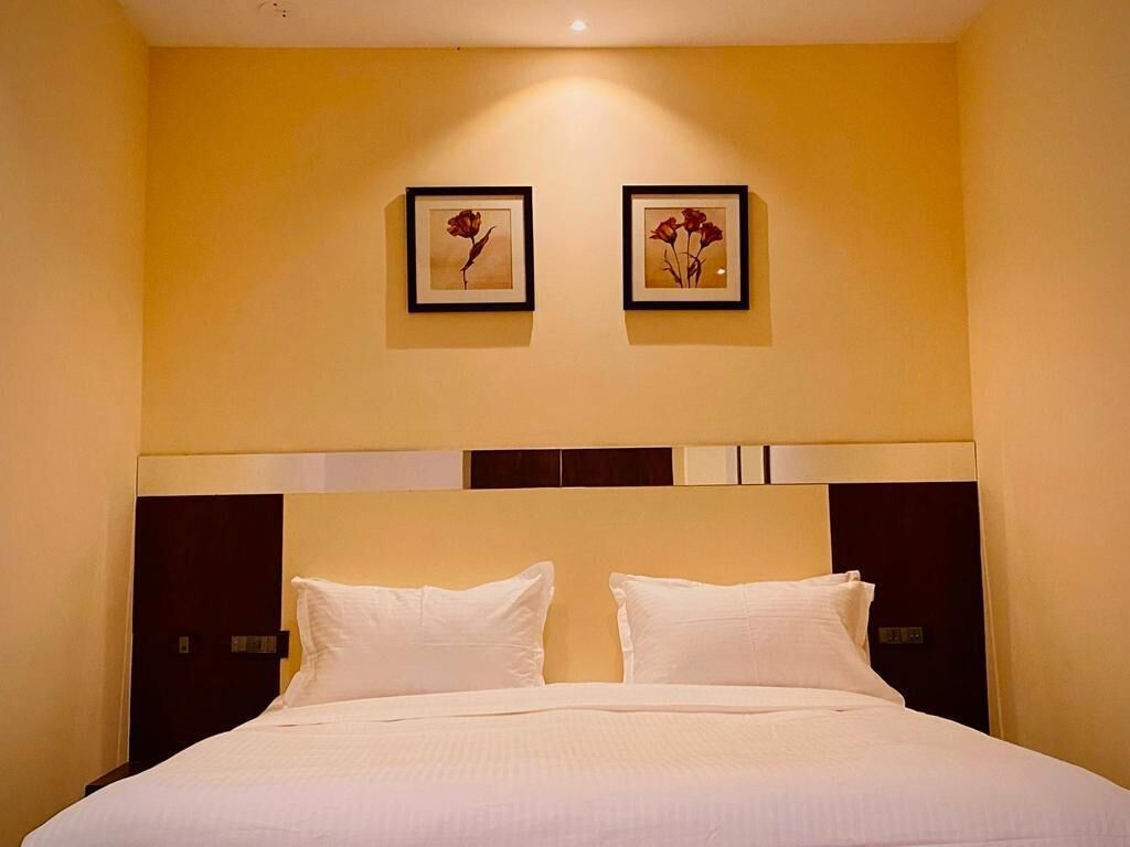 Una habitación de hotel con una cama grande, dos cuadros en la pared y un cabecero oscuro.