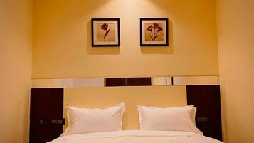 Una habitación de hotel con una cama grande, dos cuadros en la pared y un cabecero oscuro.