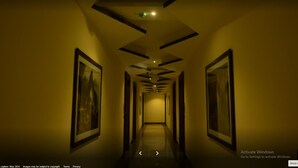 Un pasillo de hotel con cuadros enmarcados en las paredes, un techo con iluminación empotrada y un suelo que parece ser de piedra o baldosas pulidas.