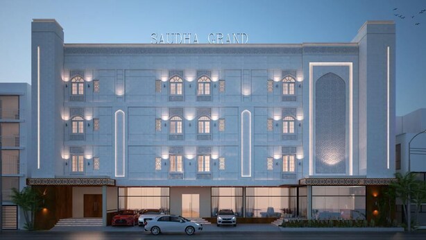 Un hotel con fachada moderna, varios balcones y una entrada destacada con autos estacionados frente a él.
