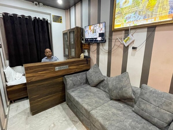 A reception area with a reception desk labeled "RECEPTION," a grey sofa with cushions, a black curtain, and a wall-mounted television displaying a map.