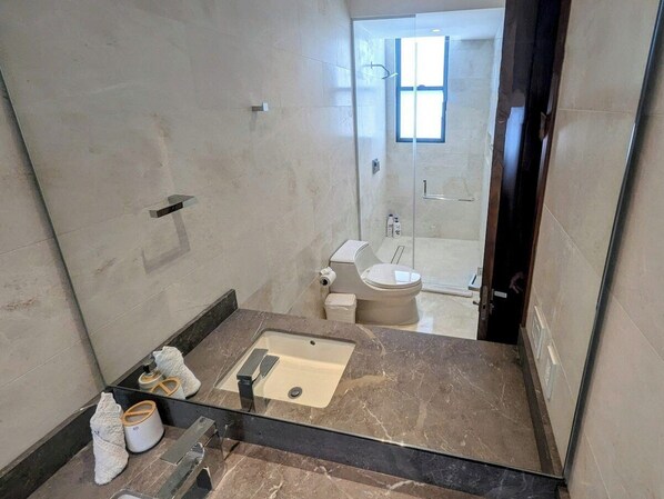 Un baño con lavamanos, inodoro y zona de ducha de mármol.