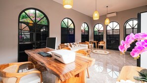 A spacious room with a wooden desk, chairs, and a sofa. There are large windows with arched tops, allowing natural light to enter. - villa koura kuta (Kuta)