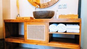 A wooden vanity with a stone basin, a woven basket, and neatly folded towels. - villa koura kuta (Kuta)