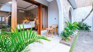 A modern bedroom with a large bed, a wooden door, and a view of the garden. - villa koura kuta (Kuta)