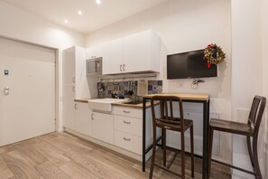 A compact kitchen with white cabinets, a tiled backsplash, a wooden countertop, and a wall-mounted TV.