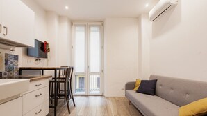 A compact living space with a kitchenette, a dining area, a sofa, and a sliding glass door leading to an outdoor balcony. - GuestHost - Lovely and cosy apartment near Porta Romana (Milano)