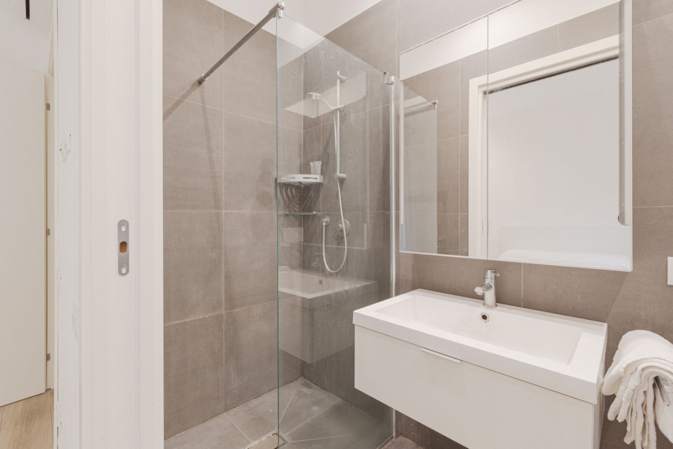 A modern bathroom with a glass-enclosed shower, a white sink, and a large mirror.