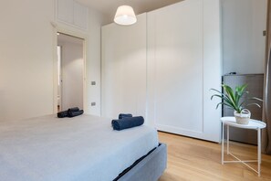 A modern bedroom with a bed, a small table with a plant, and a wardrobe.