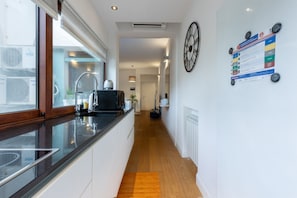 A modern kitchen with a black countertop, wooden flooring, and a clock on the wall.