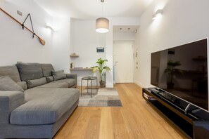 Un salón moderno con un sofá gris, suelo de madera, televisor y una pala colgada.