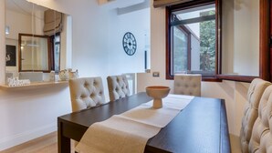 A dining area with a dark wooden table, beige upholstered chairs, a wall clock, and a window with a view of trees. - Bright apartment of about 65sqm, located on the first floor of a building with elevator (NOT suitable for disabled) can accommodate up to 2 people.Once inside you will be welcomed by a modern and comfortable, equipped with every comfort.The property is l (Cagliari)