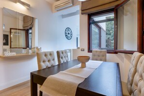 Un comedor con una mesa de madera oscura, sillas tapizadas en tonos beige, un reloj de pared y una ventana con vistas a árboles.