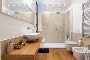 Un baño moderno con un espejo grande, un tocador de madera, una bañera independiente, cabina de ducha y un bidé.
