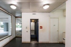Un pasillo con una puerta, un detector de incendios y una lámpara en el techo.