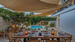 An outdoor dining area with a pool view, stone walls, and wooden furniture.