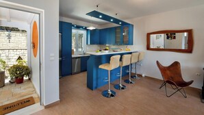A modern kitchen with blue cabinets, a central island with bar stools, and a wooden chair.