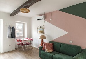 A cozy living room with a green sofa, a dining table with red chairs, and a hanging lamp. - Stresa Complex Levoasi (Stresa)