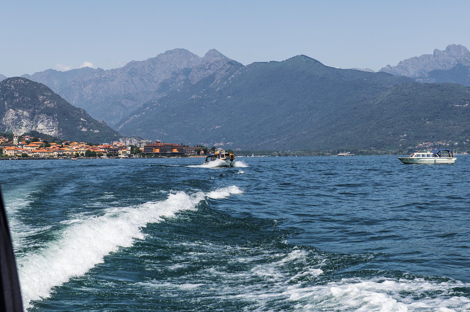 A coastal town with buildings along the waterfront, a boat in the water, and mountains in the background.
