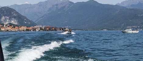 Un paese costiero con edifici lungo la passeggiata, una barca in acqua e montagne sullo sfondo.