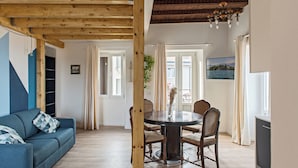 Una sala de estar con un sofá azul, una mesa de comedor de madera y sillas, y un televisor.
