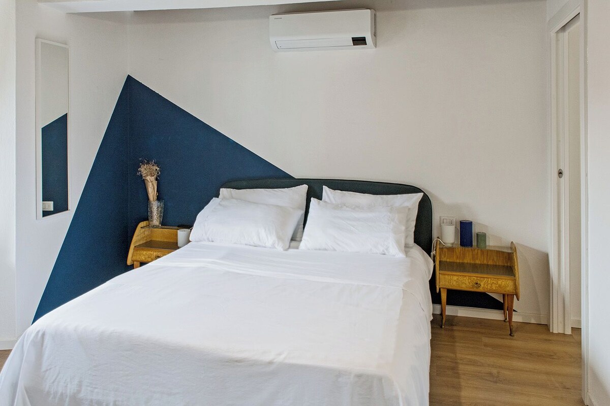 A bedroom with a bed, a nightstand, a bedside table, and a wall-mounted air conditioner.