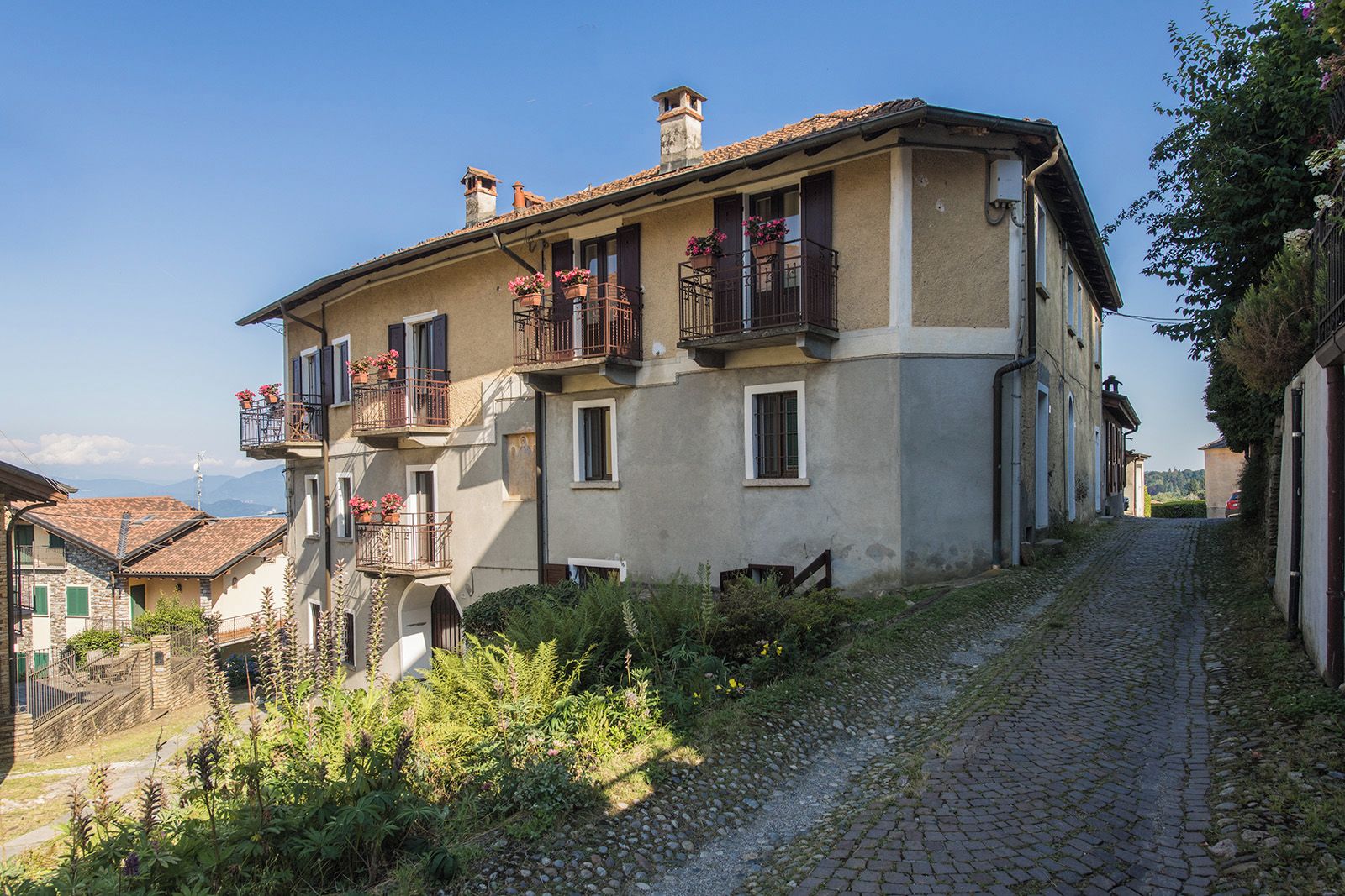 A two-story building with balconies, a cobblestone path, and surrounding greenery.