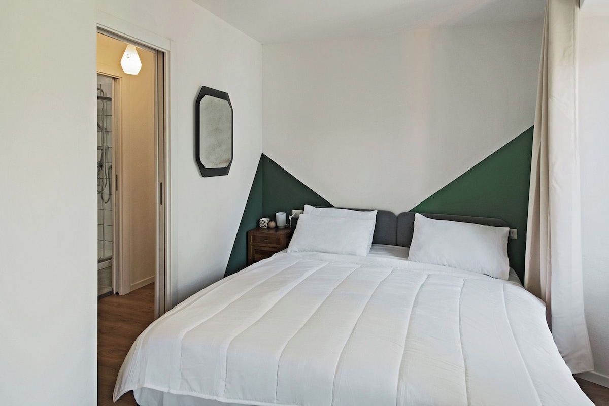 A neatly made bed with white linens, a bedside table with a lamp, and a green accent wall.