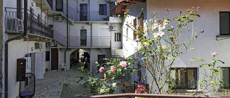 Une cour avec un sol en pierre, une rambarde en métal et un bâtiment doté de balcons et de fenêtres.
