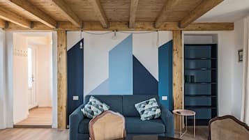 Una sala de estar moderna con un sofá azul, vigas de madera, una mesita redonda y una estantería.