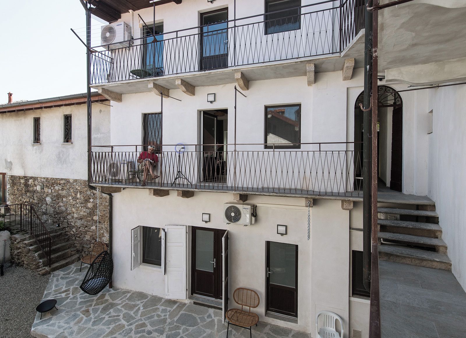 A multi-story building with balconies, a stone staircase, and outdoor seating.