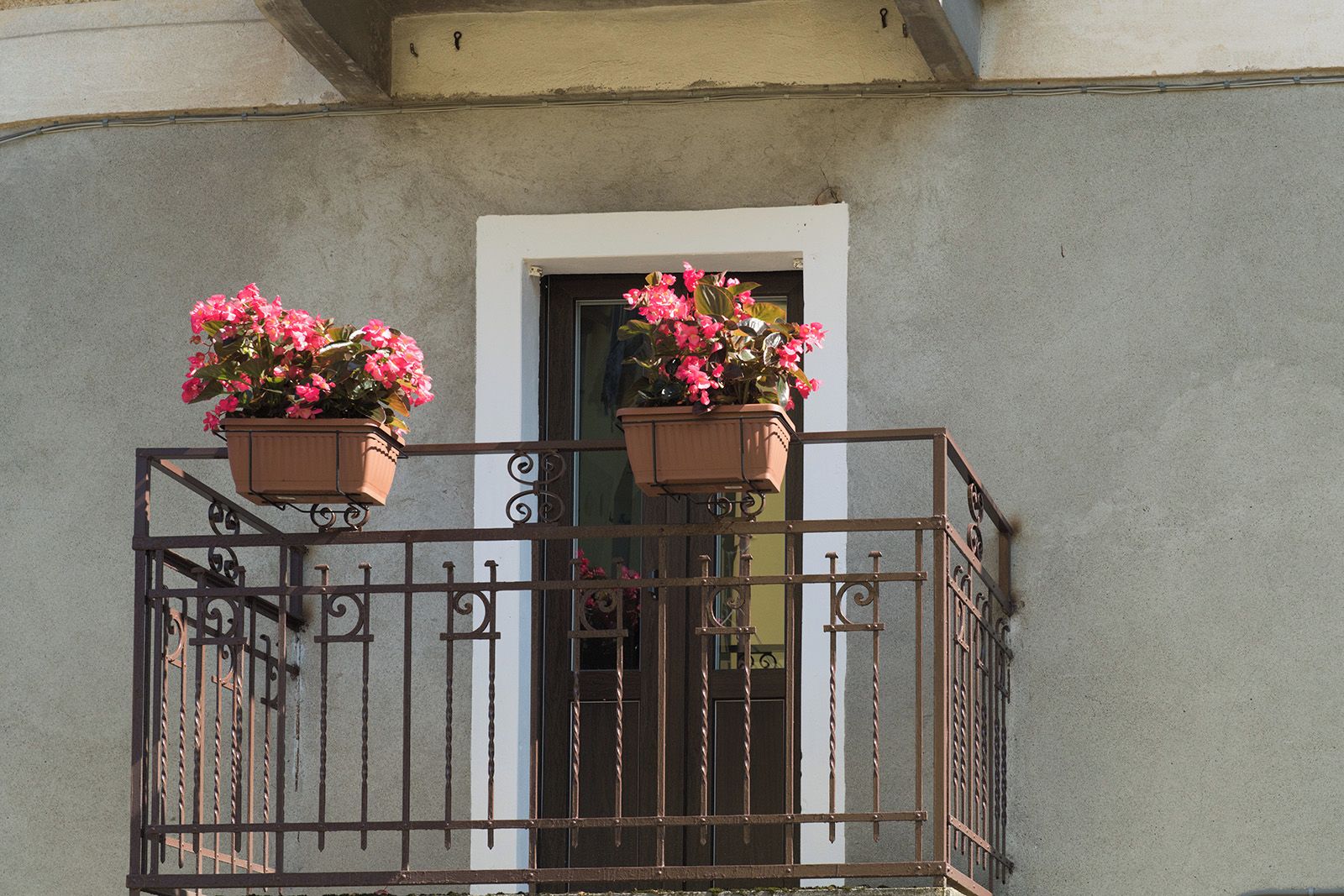 A balcony with a wrought iron railing and two flower pots with pink flowers.