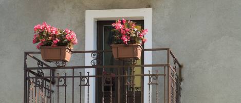 A balcony with a wrought iron railing and two flower pots with pink flowers.