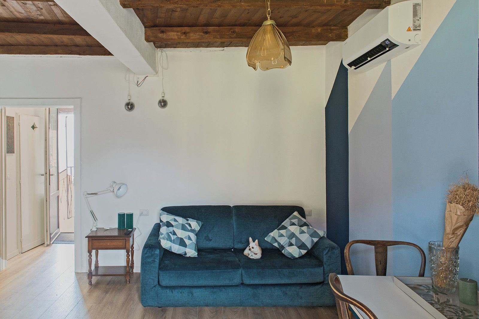 Ein gemütliches Wohnzimmer mit einem blauen Sofa, einem kleinen Tisch und einer Pendelleuchte.