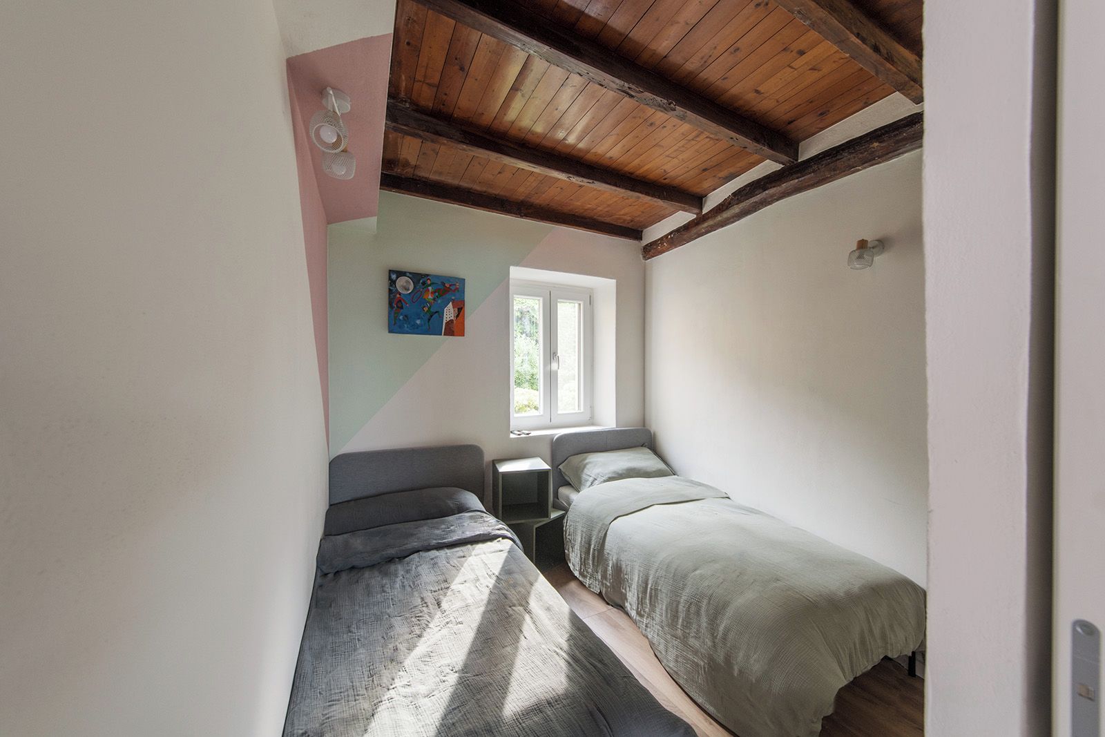 Een kleine, smalle kamer met twee bedden, een raam en een schilderij aan de muur.