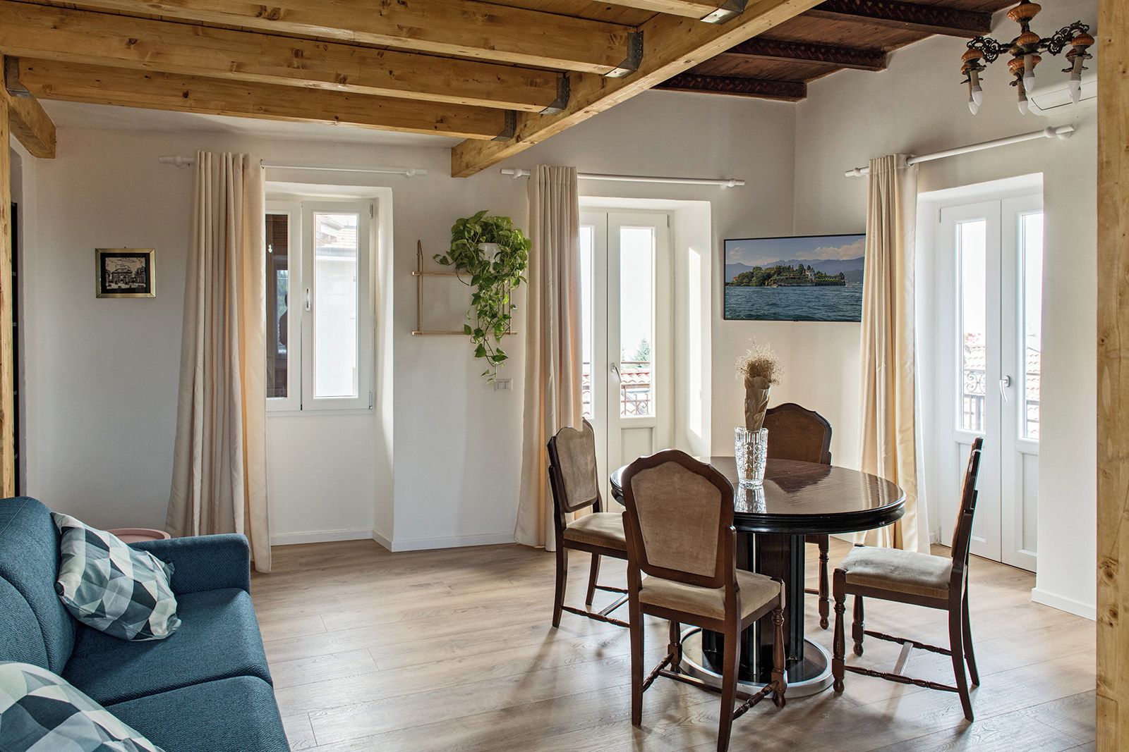 A cozy living room with a wooden ceiling, a dining table with chairs, a blue sofa, and a painting on the wall.