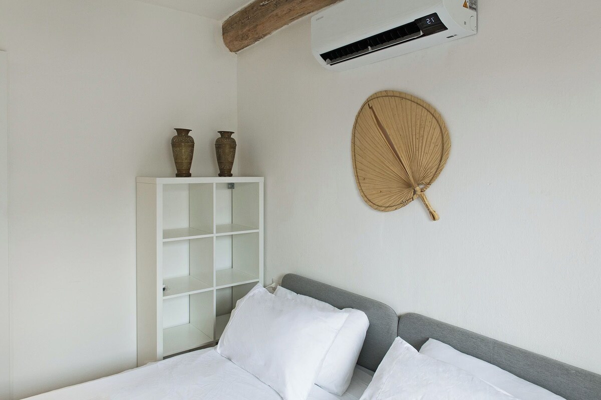 Quarto com cama, guarda-roupa branco e ventoinha na parede.