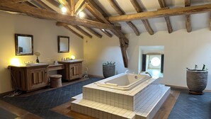 A bathroom with a large bathtub, wooden beams, a mirror, and a sink.