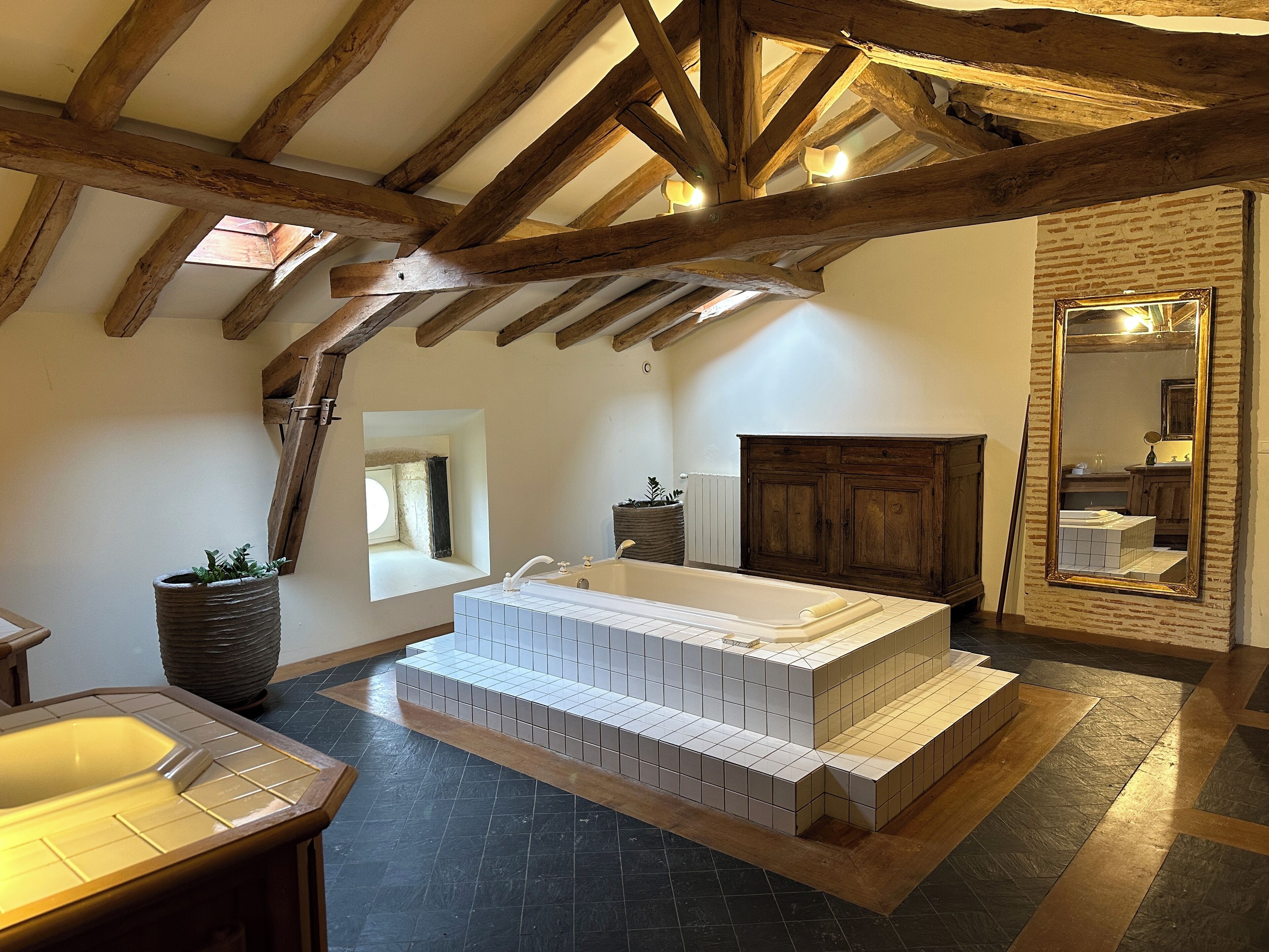 A bathroom with a large bathtub, wooden beams, a mirror, and a potted plant.