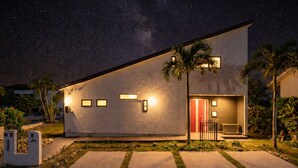 A modern house with a large balcony, a red door, and a starry night sky. - 1688 House Churaumi (Motobu)