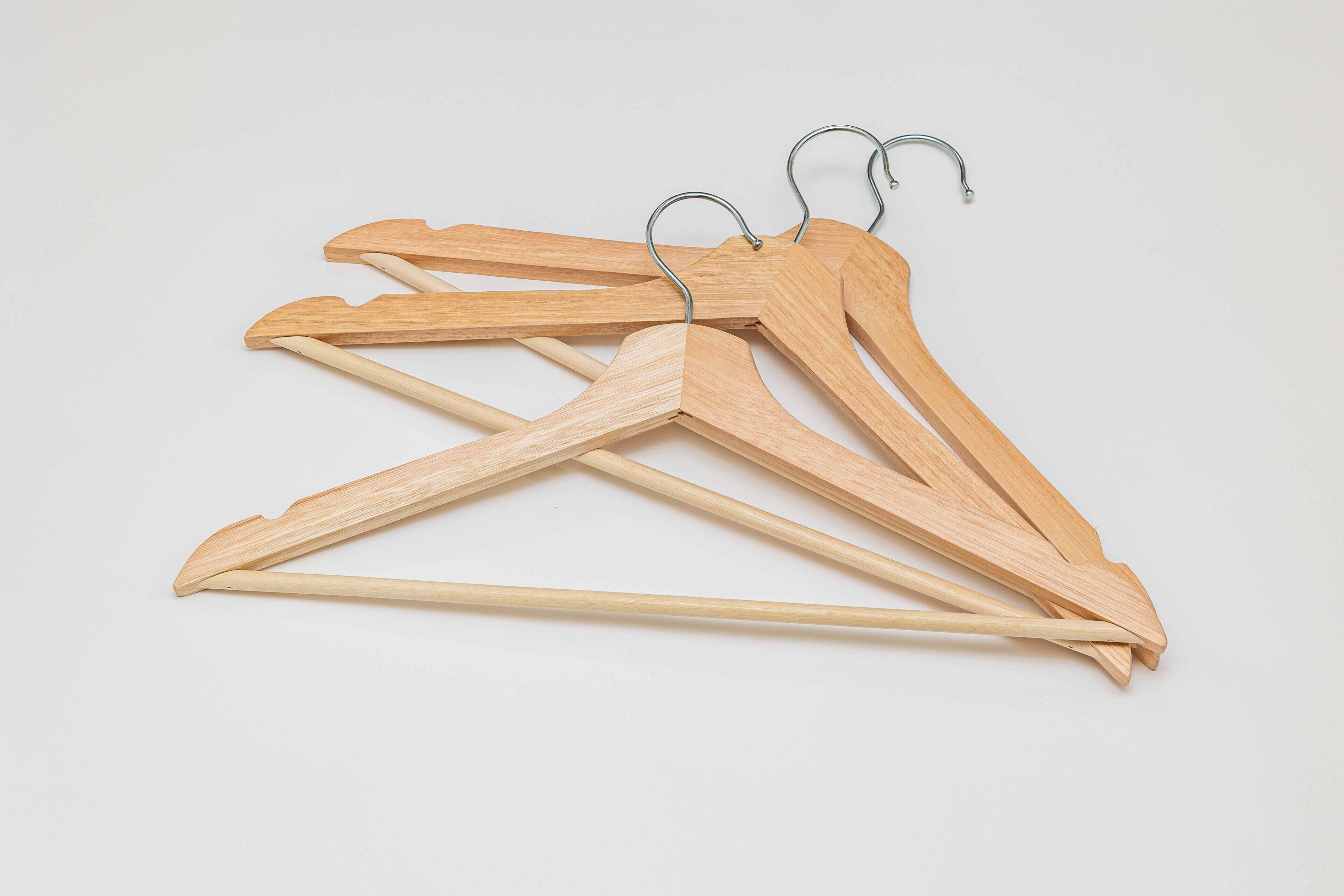 Three wooden hangers with metal hooks on a plain background.