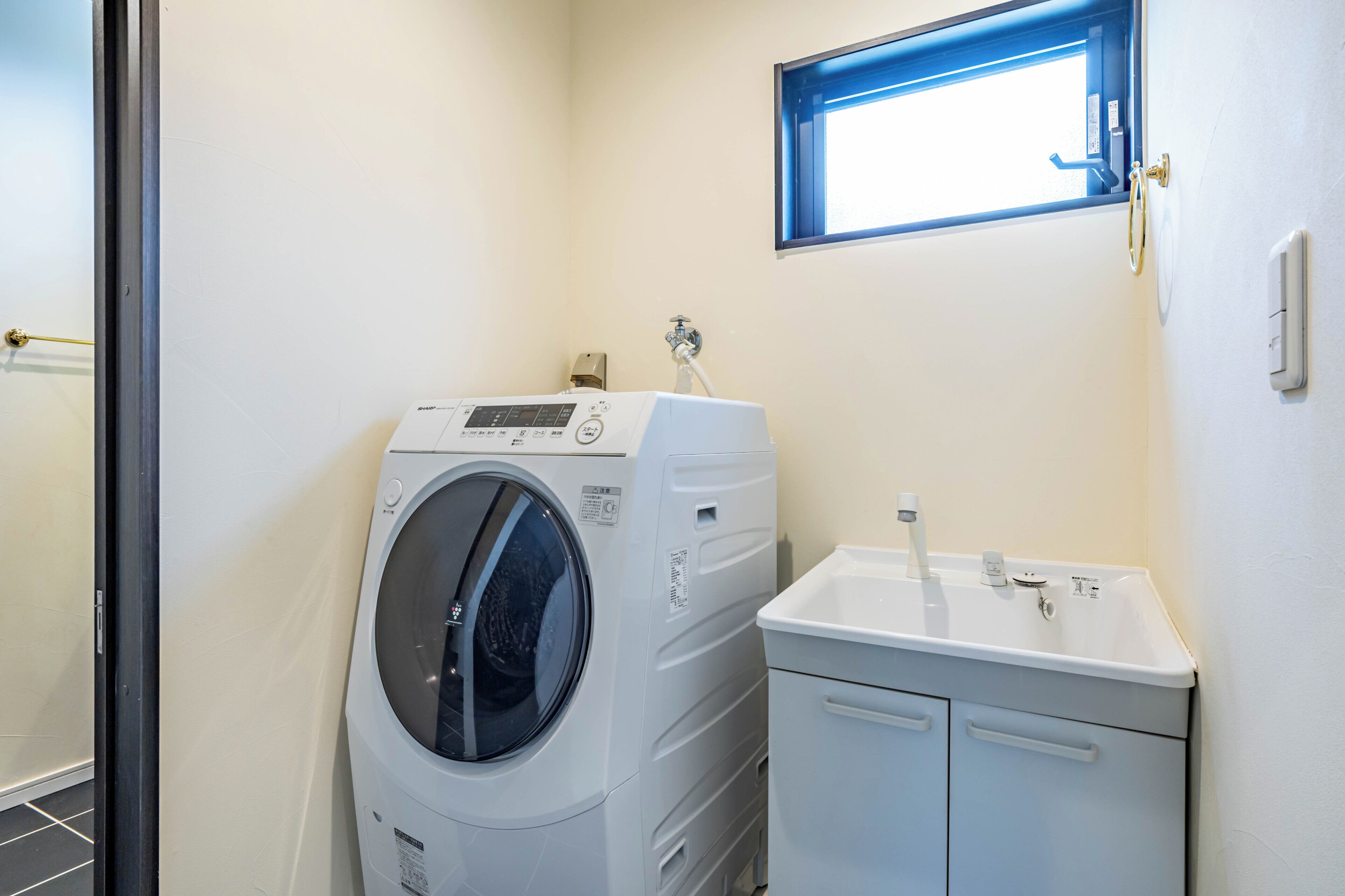 A laundry room with a front-loading washing machine, a sink, and a window above the sink.