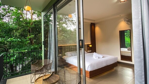 Une chambre moderne avec un grand lit, un balcon avec des chaises et une vue sur la verdure.