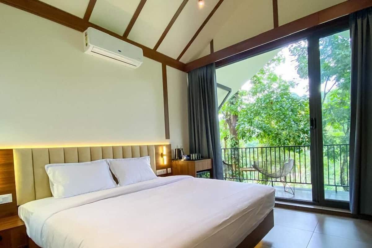 Quarto de hotel moderno com uma cama grande, uma varanda com vista para o verde e teto com vigas de madeira.