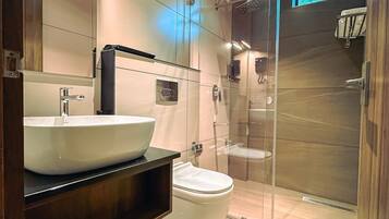 Un baño moderno con un lavamanos grande tipo cuenca, un inodoro y una zona de ducha con mampara de vidrio.