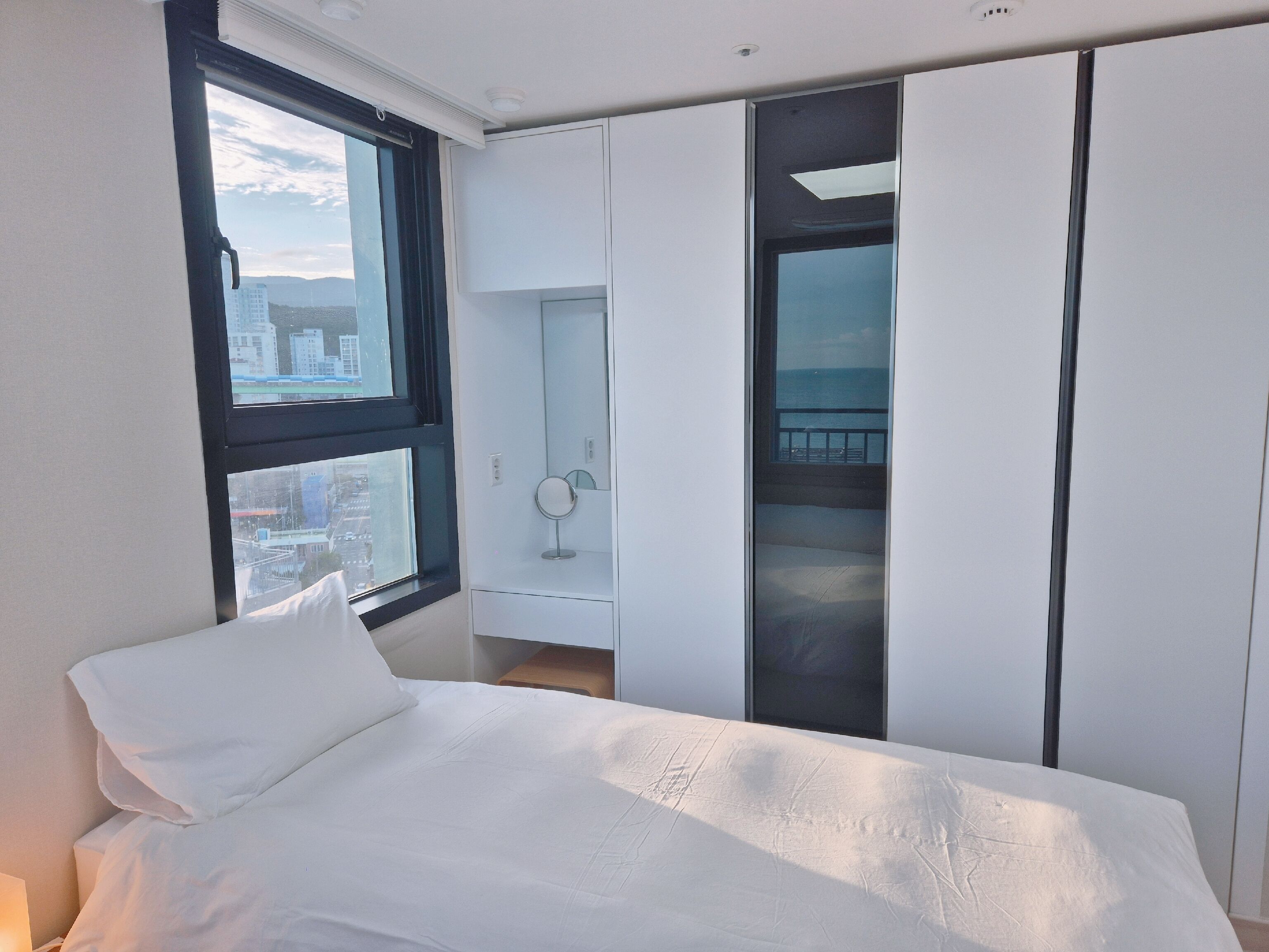 Een moderne slaapkamer met een groot bed, een inloopkast en uitzicht op de stad door een raam.