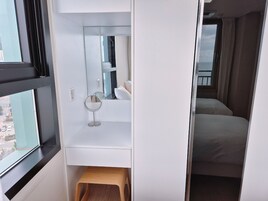 Habitación de hotel con un ventanal grande, un taburete de madera, un espejo redondo y una cama con cortina.