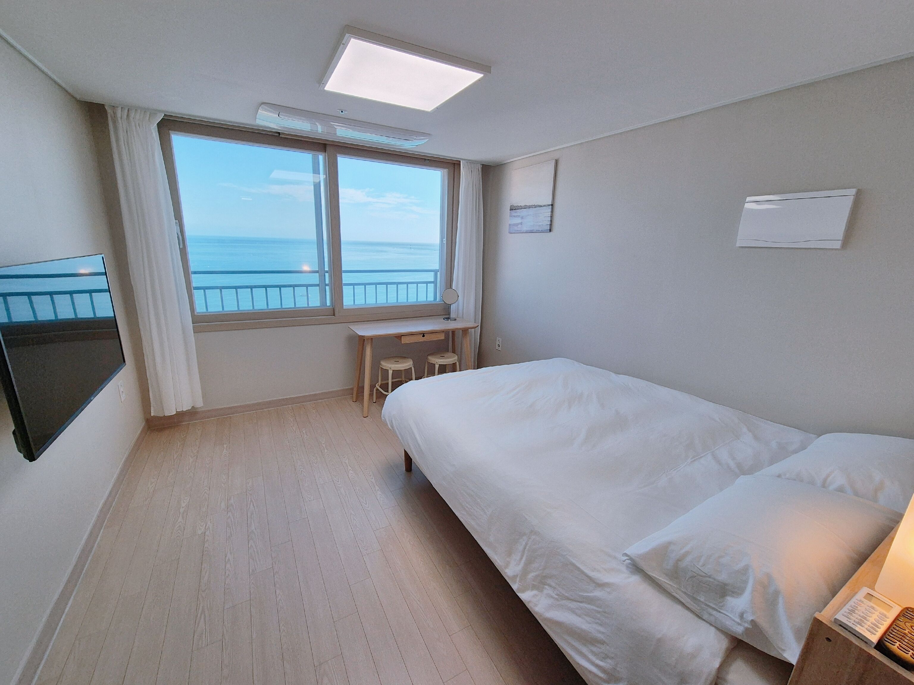 A hotel room with a bed, a desk, a chair, a TV, and a window with a view of the sea.
